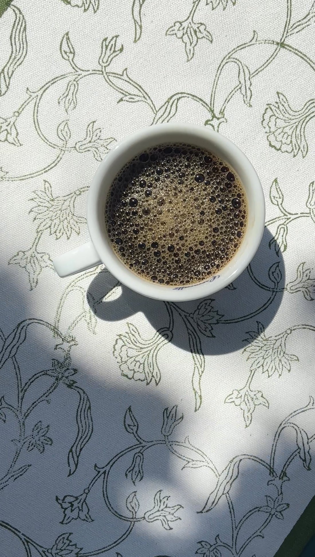 a cup of black coffee on a floral printed table runner in green