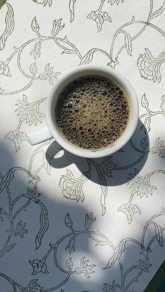 a cup of black coffee on a floral printed table runner in green